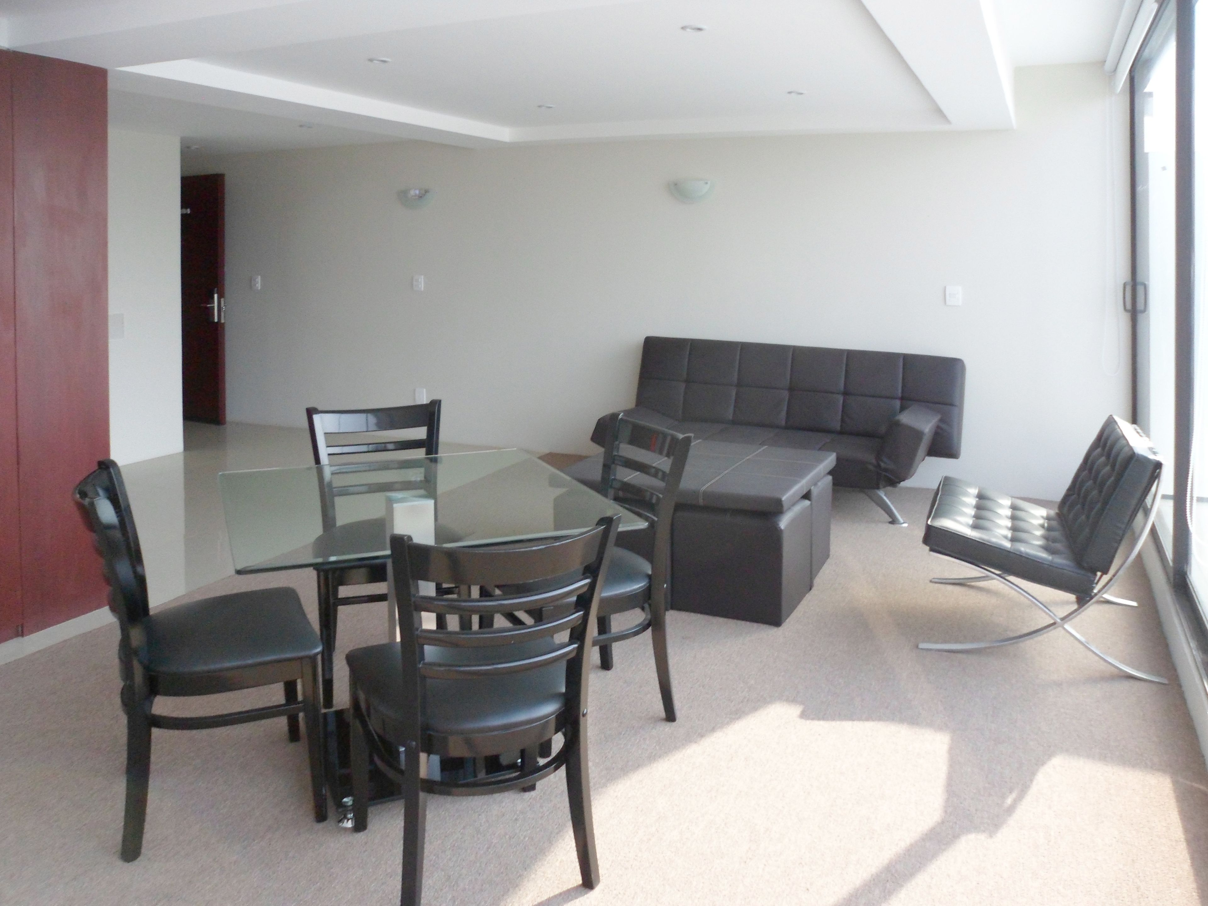 Una sala de estar moderna con una mesa de comedor de cristal, sillas negras, un sofá gris y un sillón negro.