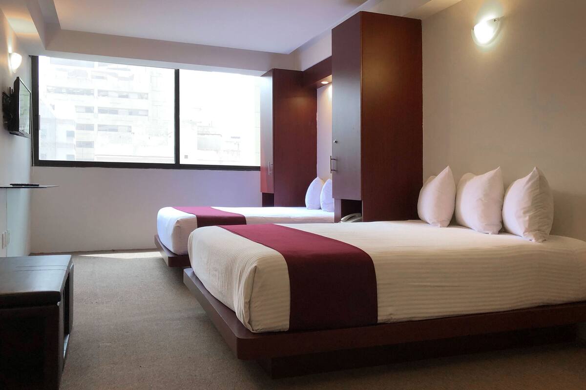 Ein modernes Hotelzimmer mit einem großen Bett, einem Nachttisch, einem Kleiderschrank und einem Fenster mit Blick auf die Stadt.