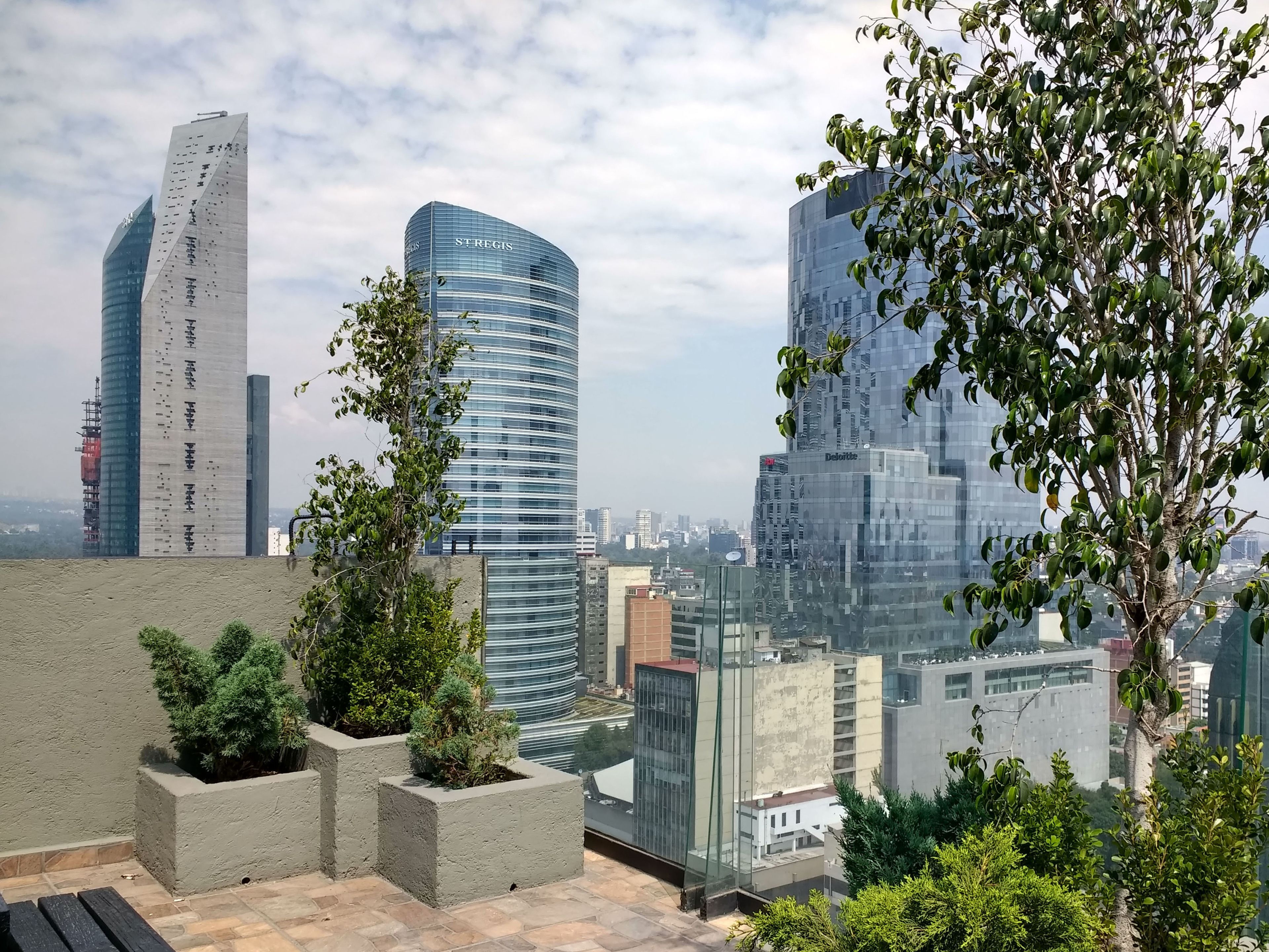 A modern cityscape with high-rise buildings, including a curved glass structure and a tall rectangular building with signage.