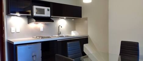 A modern kitchen with a built-in microwave, a sink, and a glass dining table with chairs.