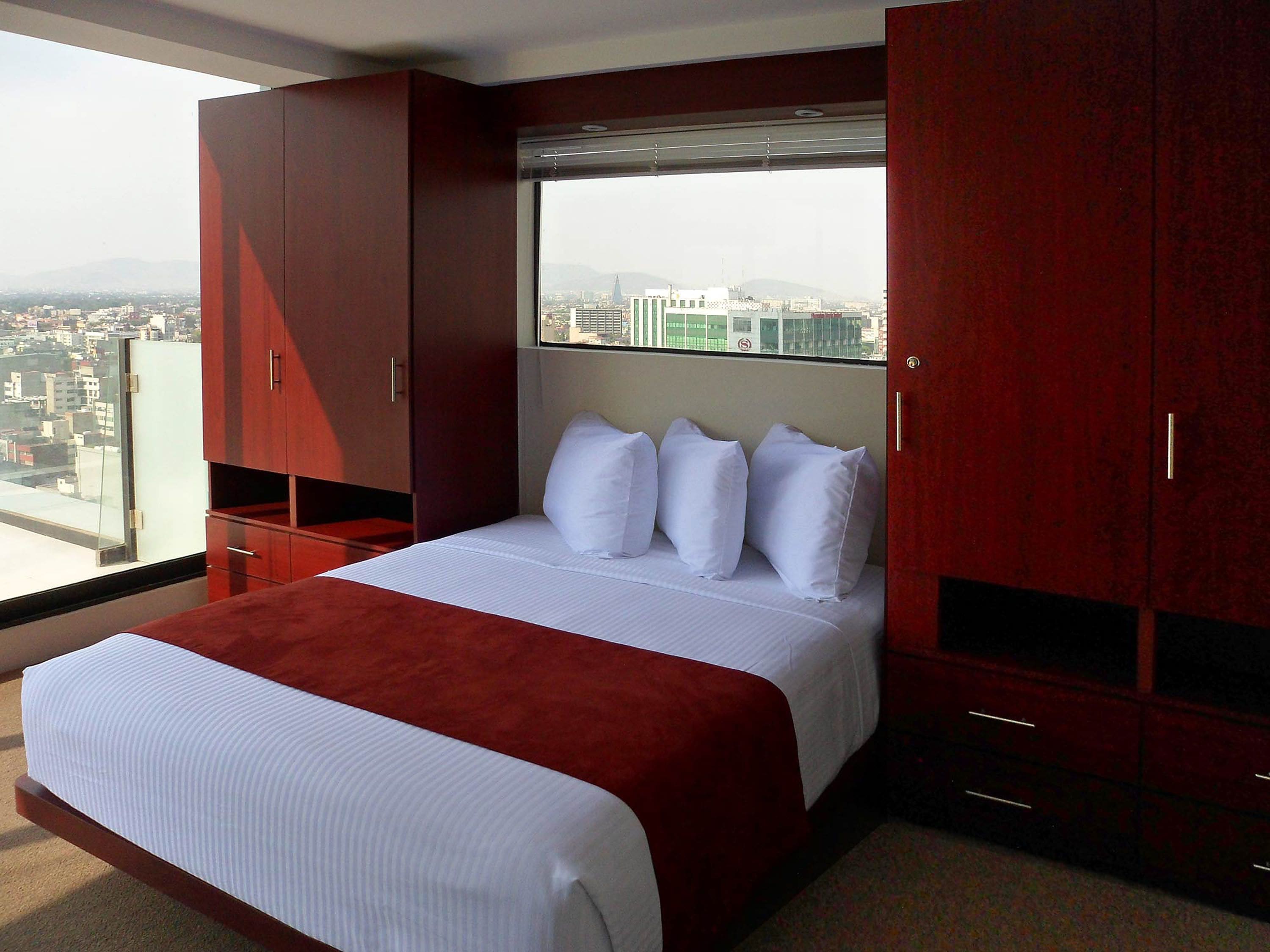 Une chambre d’hôtel moderne avec un grand lit, une vue sur la ville et une armoire rouge.