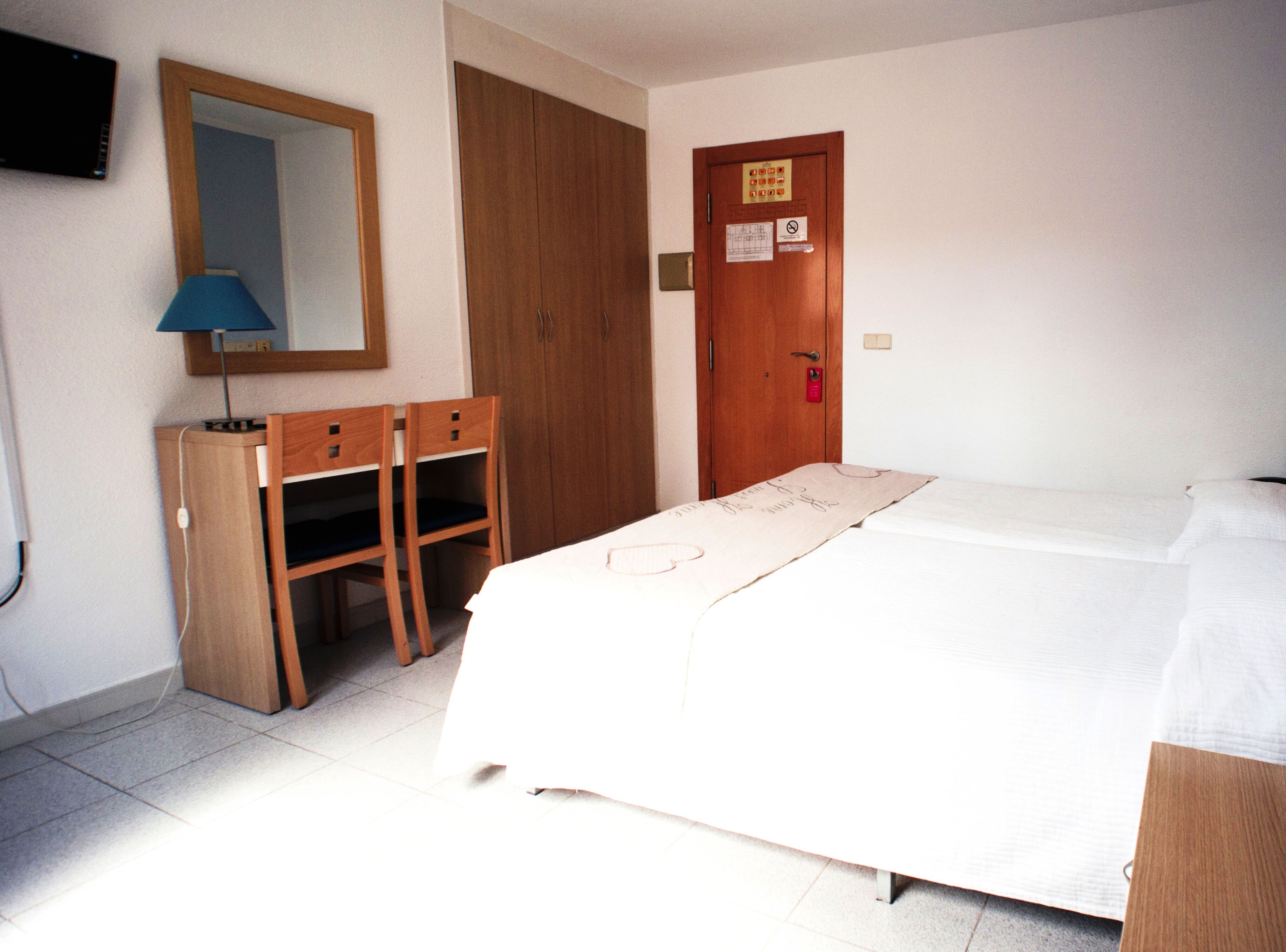 Ein Hotelzimmer mit einem Bett, einem Schreibtisch mit Stühlen, einem Spiegel und einem Kleiderschrank.