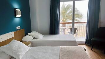 Une chambre d’hôtel avec deux lits, une table de chevet, une chaise et un balcon donnant sur des palmiers.