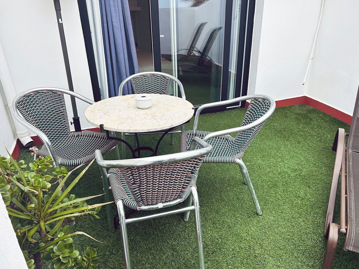 A small patio area with a round table and four wicker chairs, surrounded by artificial green grass.