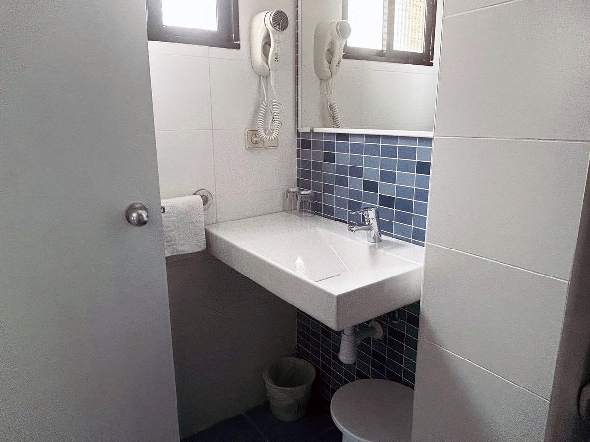 Ein kleines Badezimmer mit einem weißen Waschbecken, einem Spiegel und einem an der Wand montierten Fön.