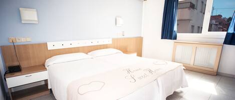 Habitación de hotel ordenada con cama, mesita de noche y ventana con cortinas.
