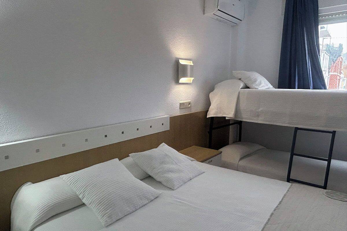 Una habitación de hotel con una cama litera, una cama individual y una mesita de noche.