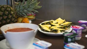 A kitchen counter with a bowl of soup, a plate of sliced fruit, and several containers of yogurt.