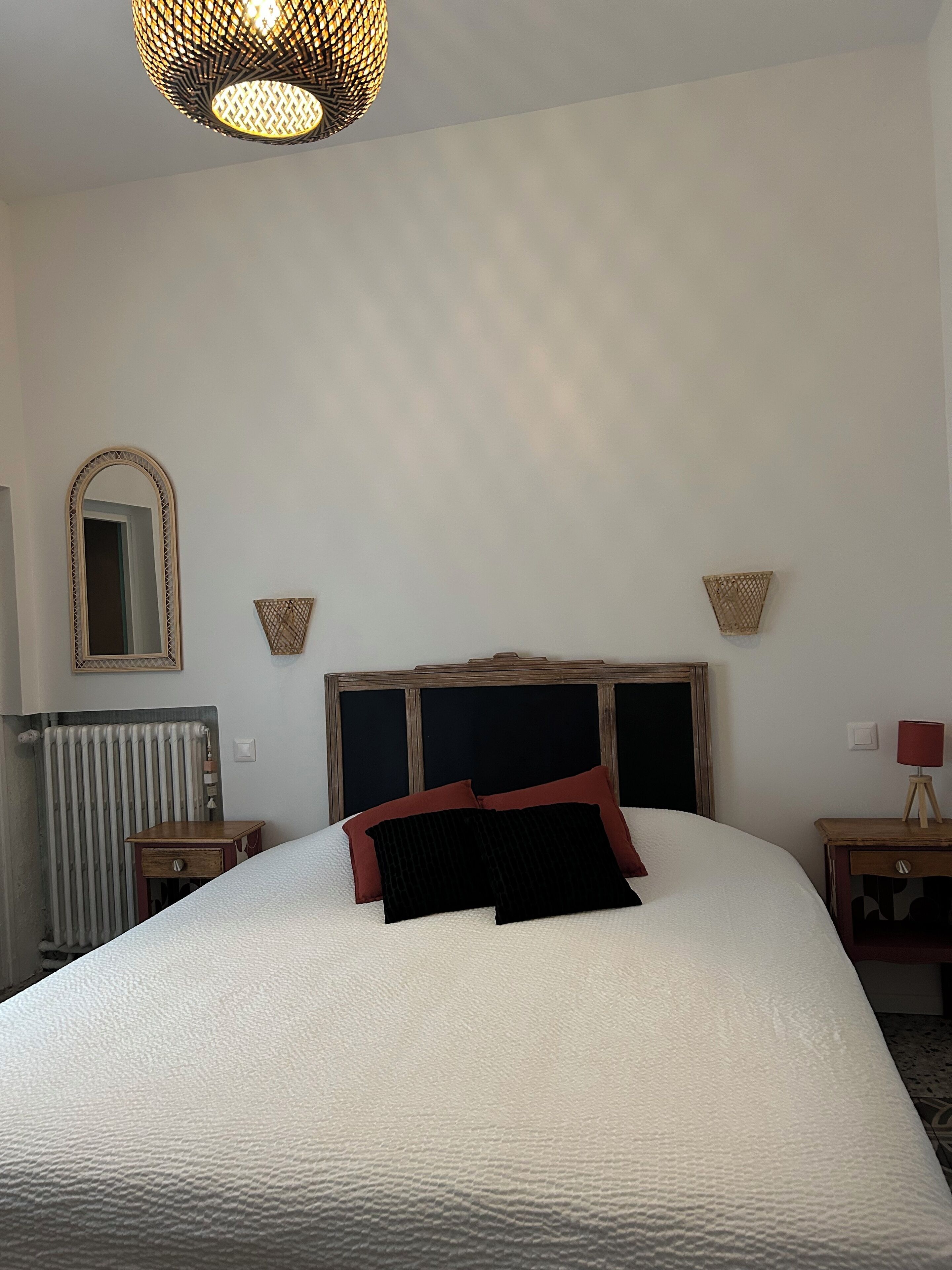 A neatly arranged bedroom with a large bed, a wooden headboard, a mirror, and two bedside tables with lamps.