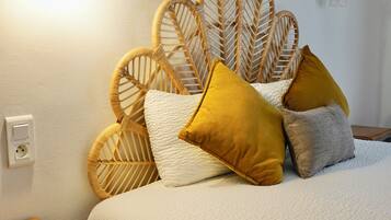 A neatly made bed with a white textured bedspread, a wicker headboard, and several pillows in mustard and grey colors.