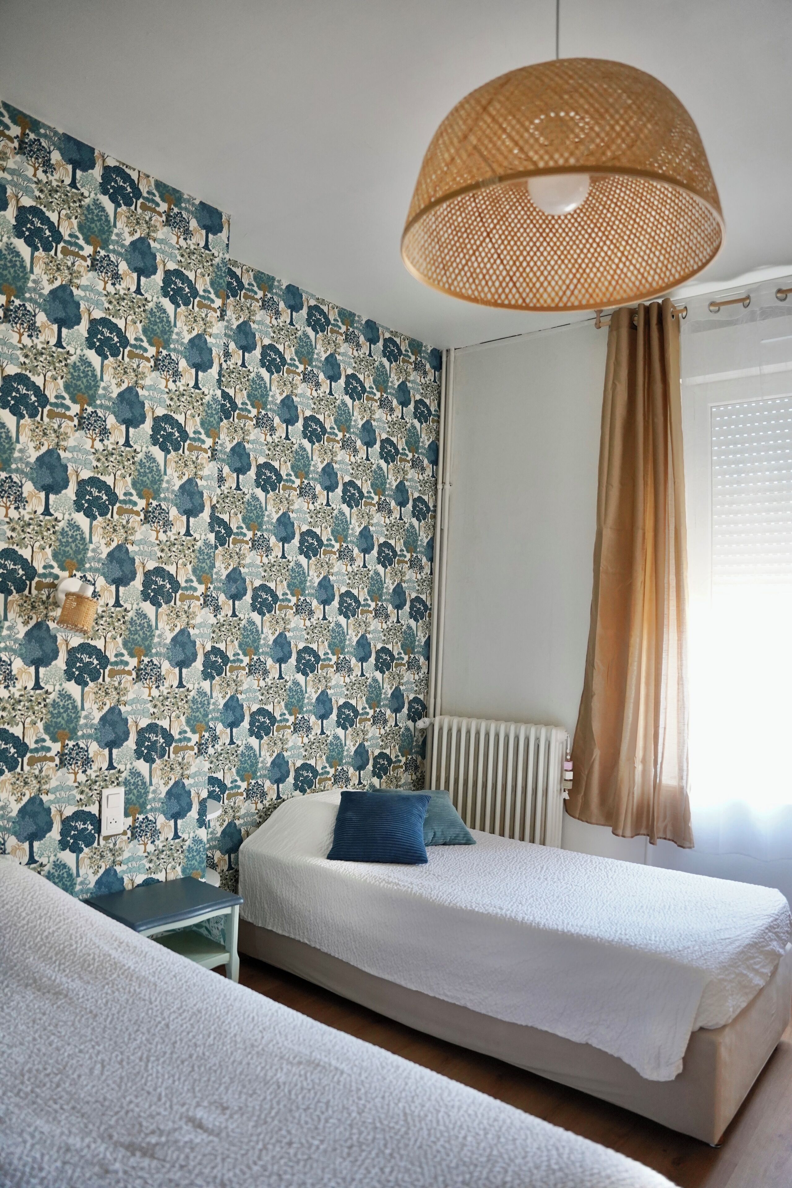 A bedroom with a patterned wallpaper, a bed with a white cover, a bedside table, and a hanging lamp.