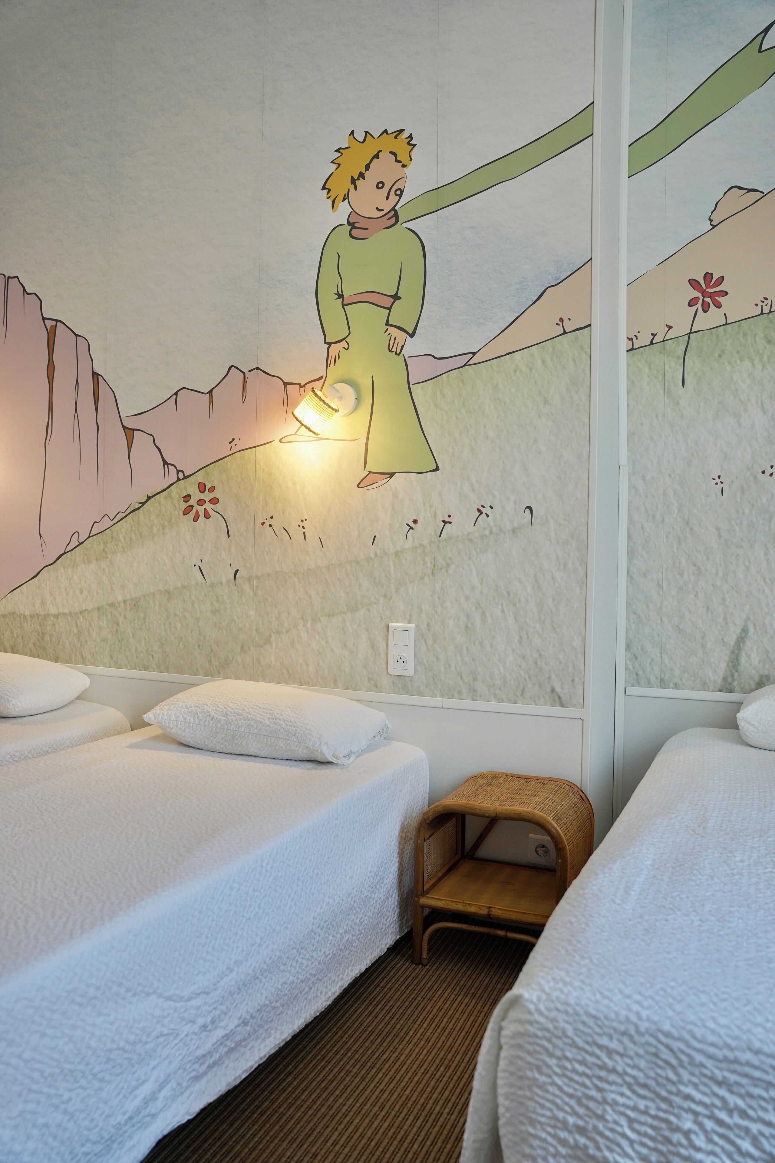 Une chambre d’hôtel avec deux lits, une fresque murale et une petite chaise en bois.