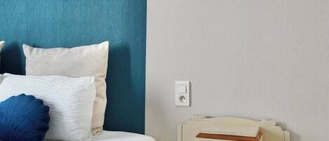 A neatly made bed with white and blue bedding, a bedside table with a drawer, and a wall-mounted light fixture.
