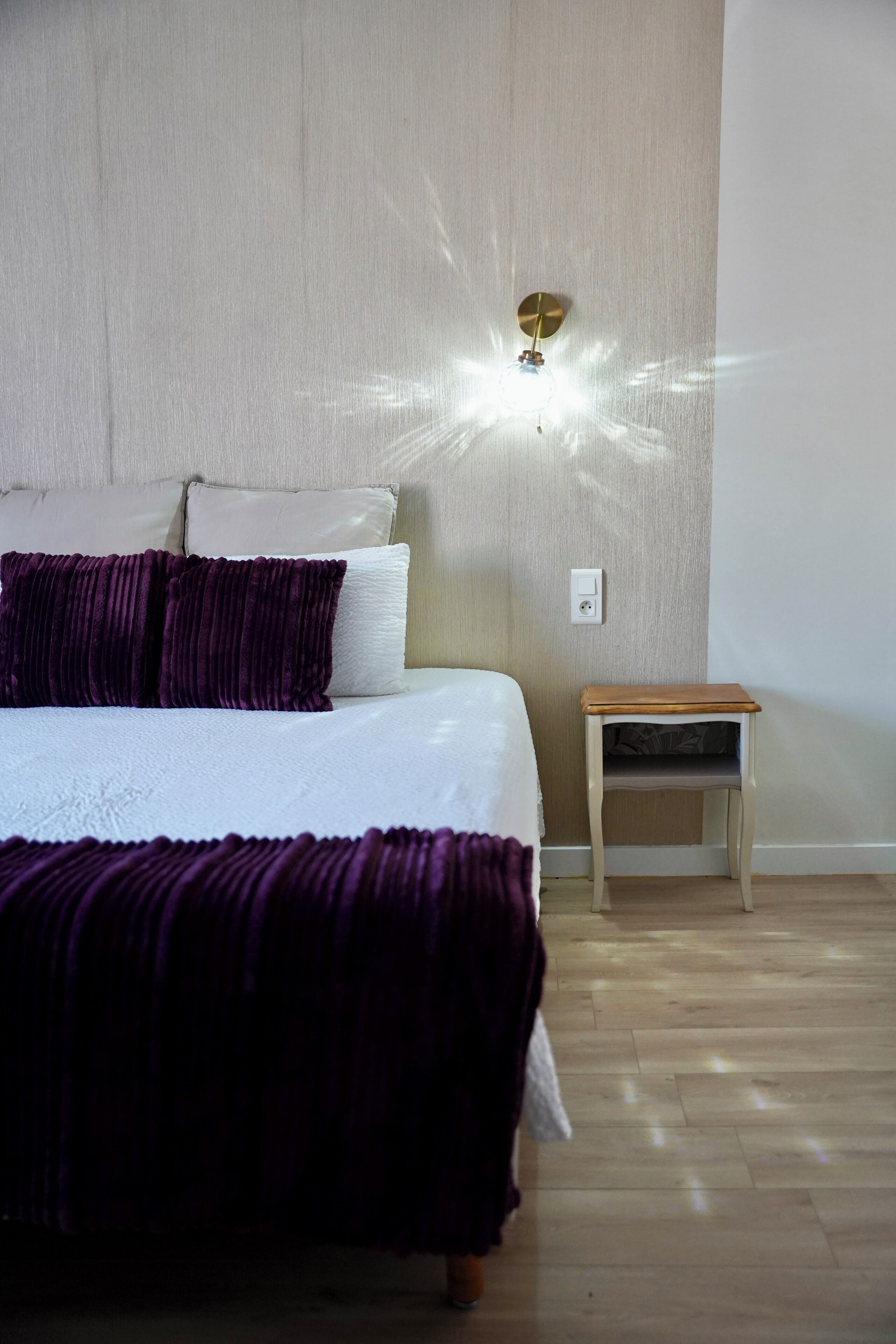 A bedroom with a bed, pillows, a nightstand, and a wall-mounted light fixture.