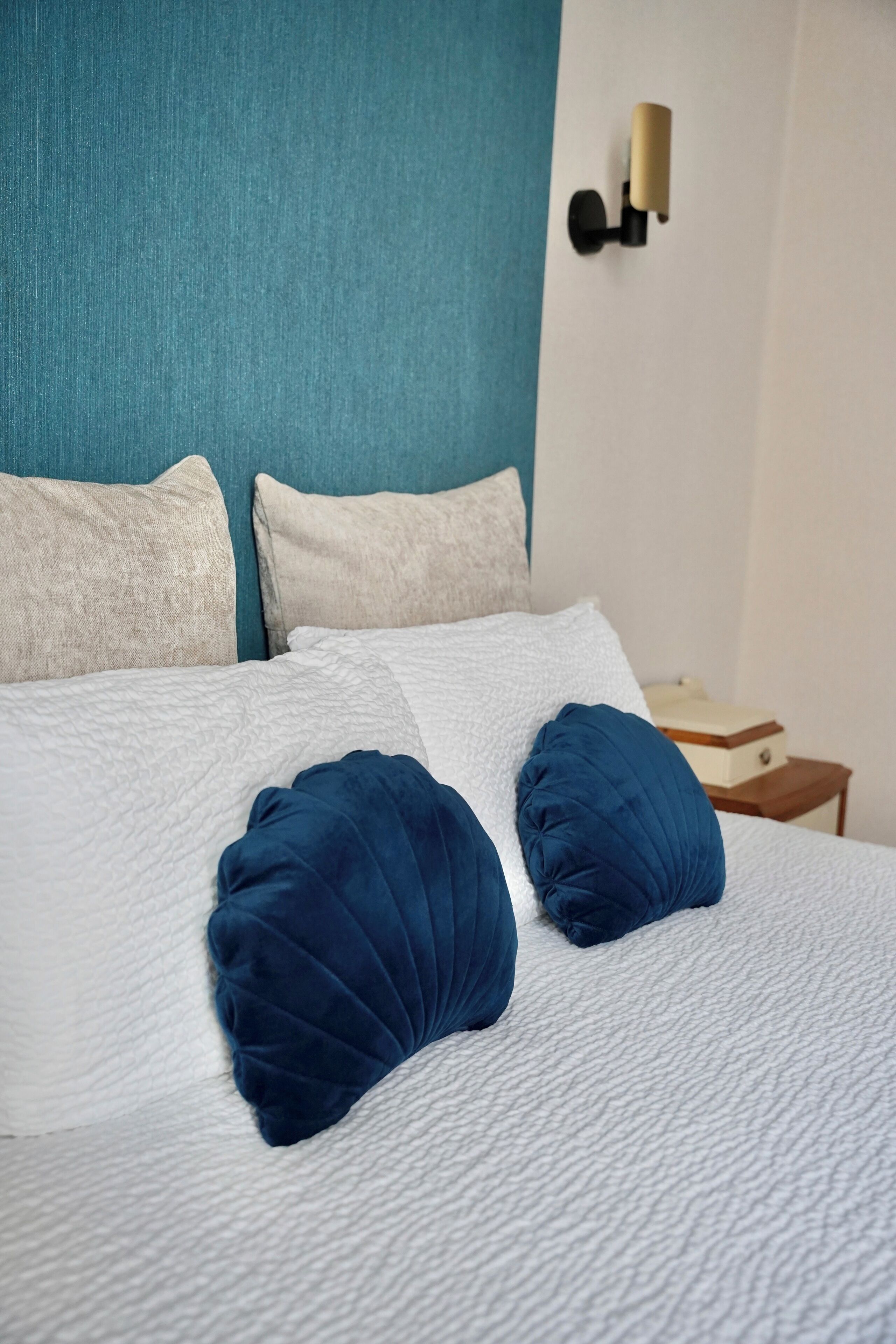 A neatly made bed with white and blue bedding, a teal headboard, and a small bedside table with a lamp.