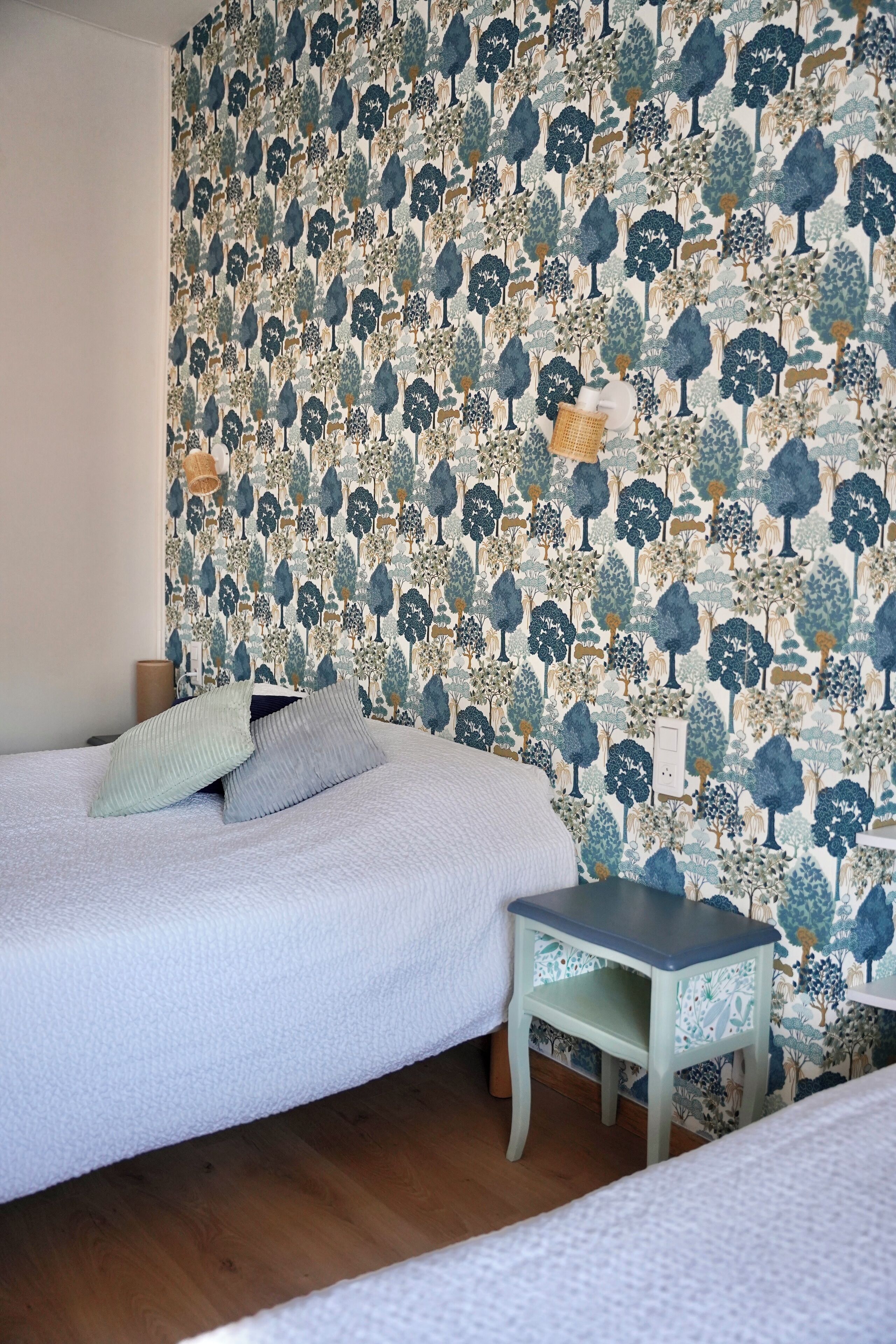 Una camera da letto con carta da parati decorata, un letto con cuscini, un comodino e una abat-jour.