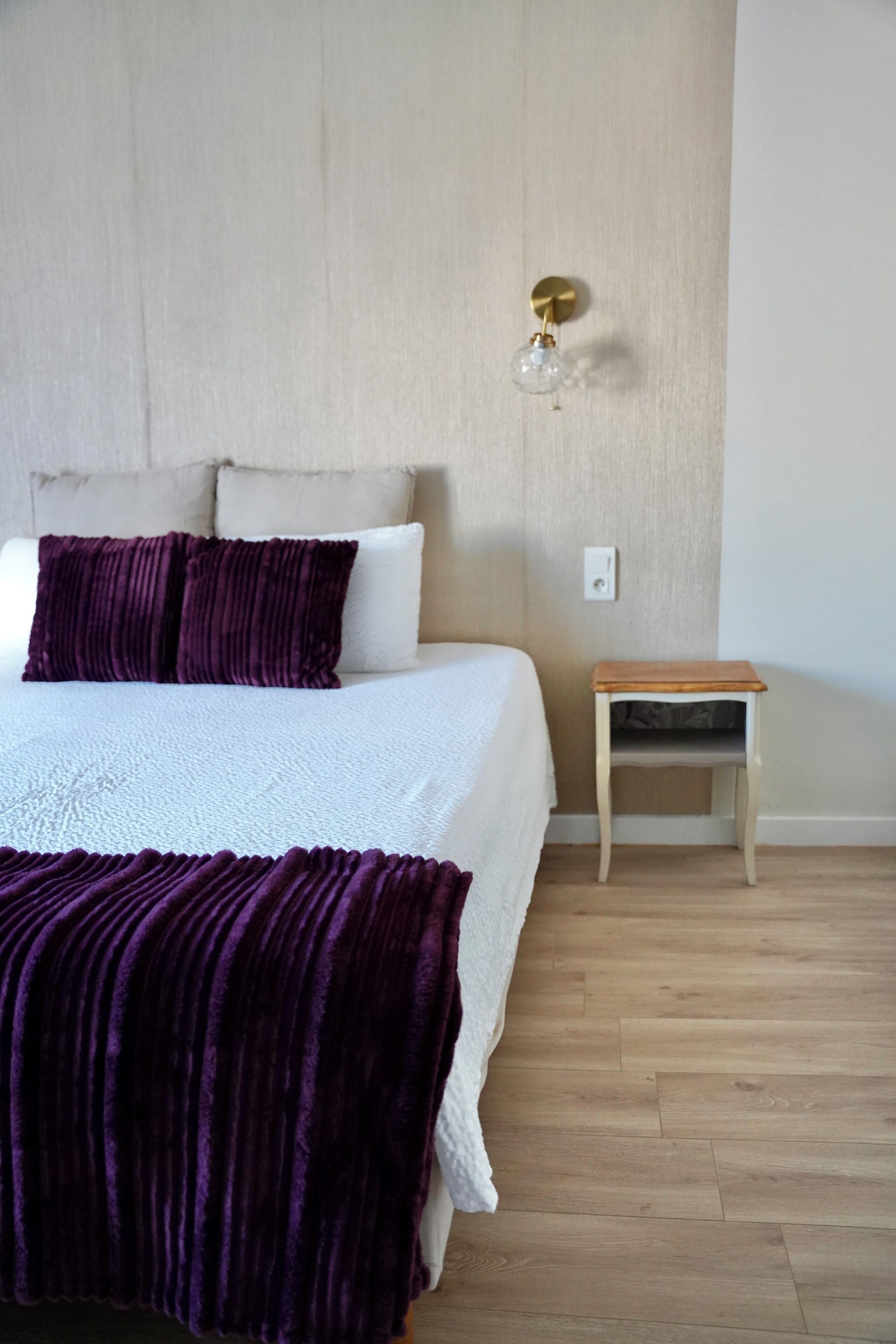 Un dormitorio con cama, mesita de noche y lámpara fijada a la pared.
