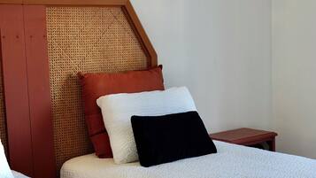 Une chambre avec deux lits, une tête de lit en bois, une petite table de chevet et un luminaire fixé au mur.