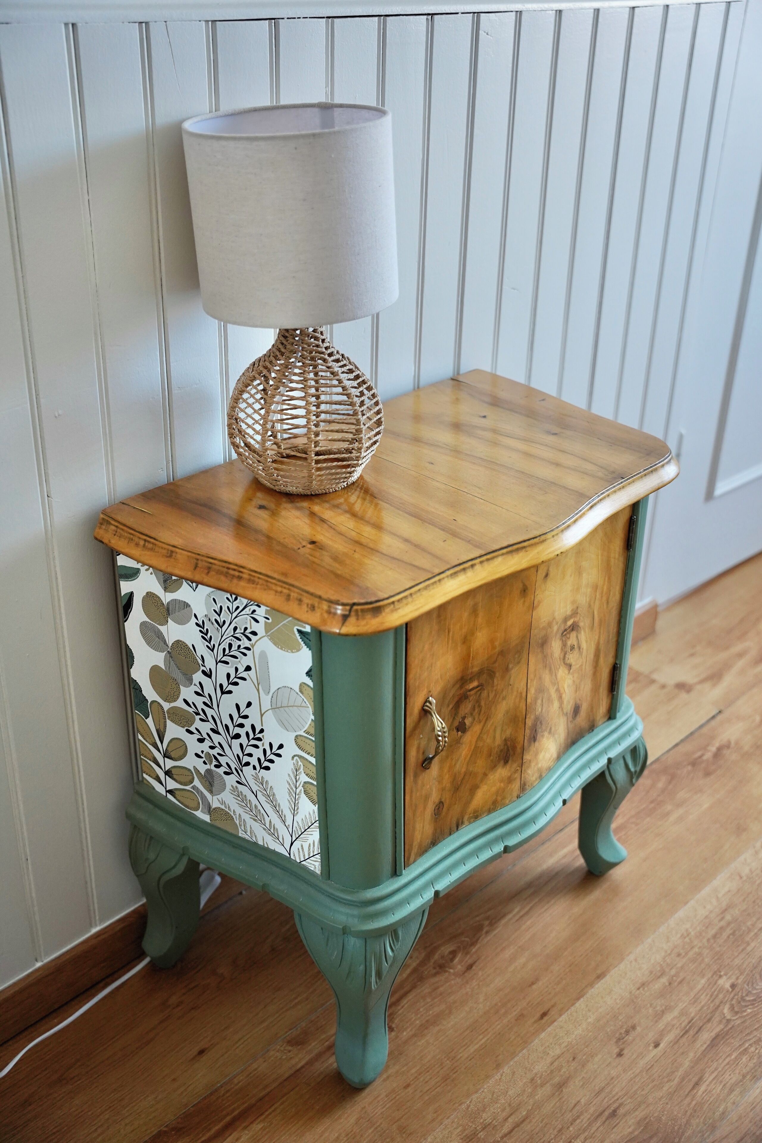 Une table d’appoint en bois, de style vintage, agrémentée d’un abat-jour tissé, d’un panneau décoratif et d’un tiroir.