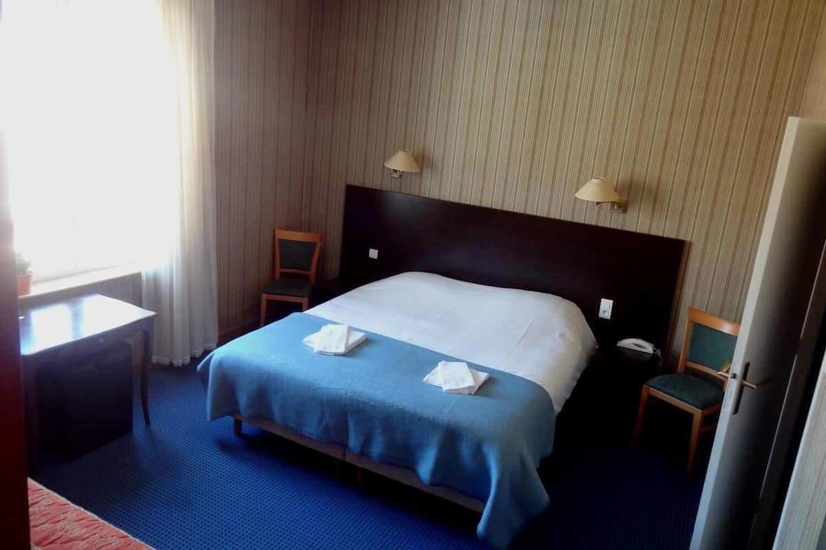 A hotel room with a bed, two chairs, a desk, a lamp, and a TV.