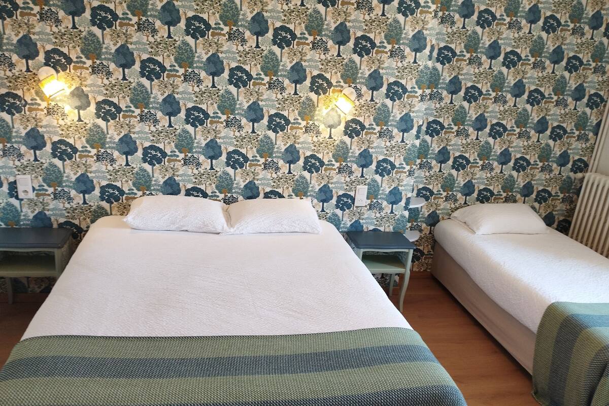 A room with two beds, a small table, and a patterned wallpaper.