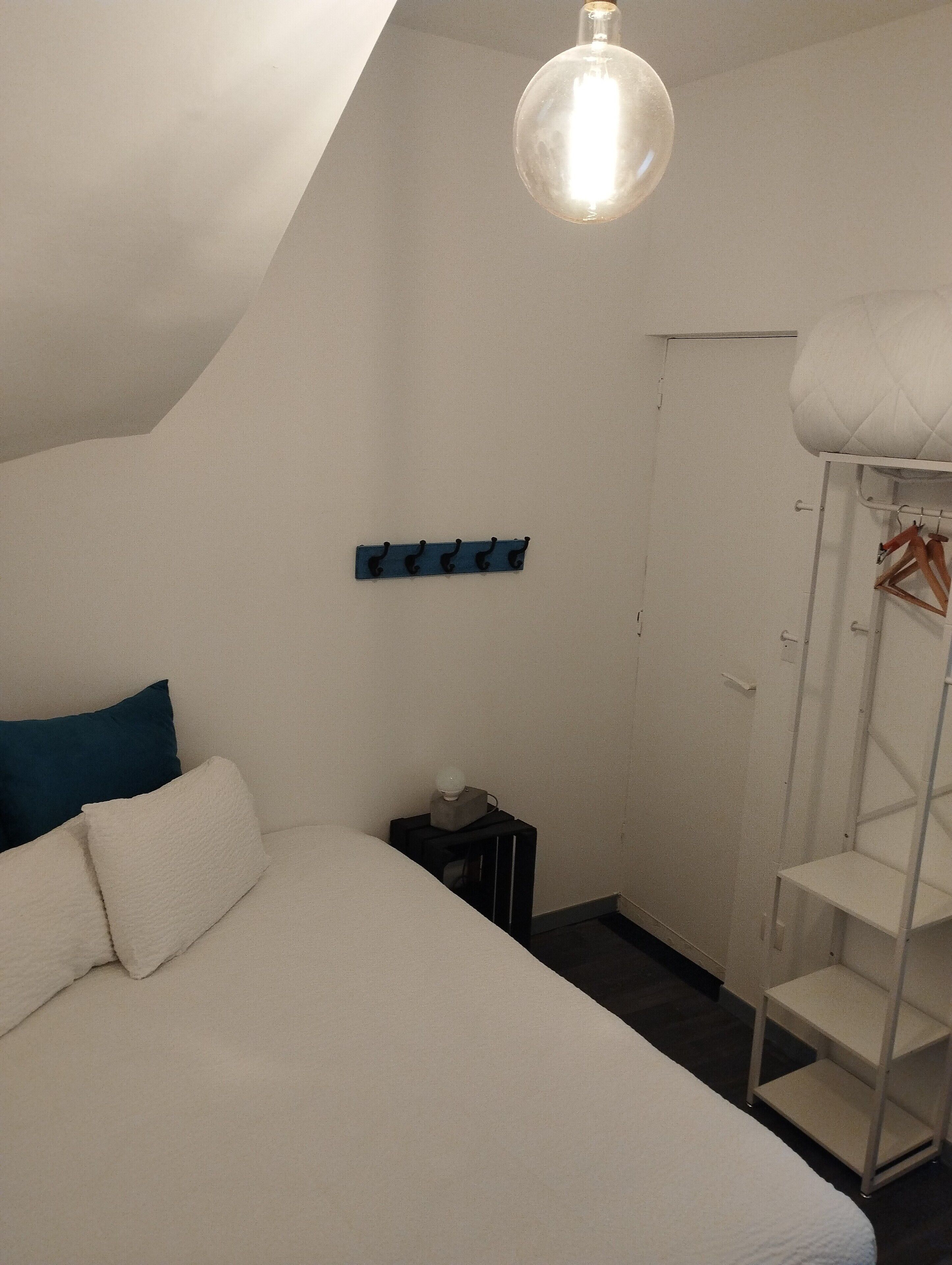 A bedroom with a bunk bed, a bedside table, a lamp, a wardrobe, and a shelf with hooks.