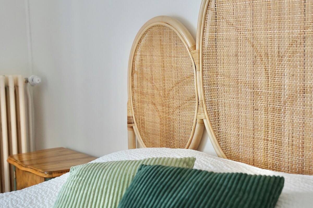 A bed with a white textured mattress, two green pillows, and a wicker headboard.