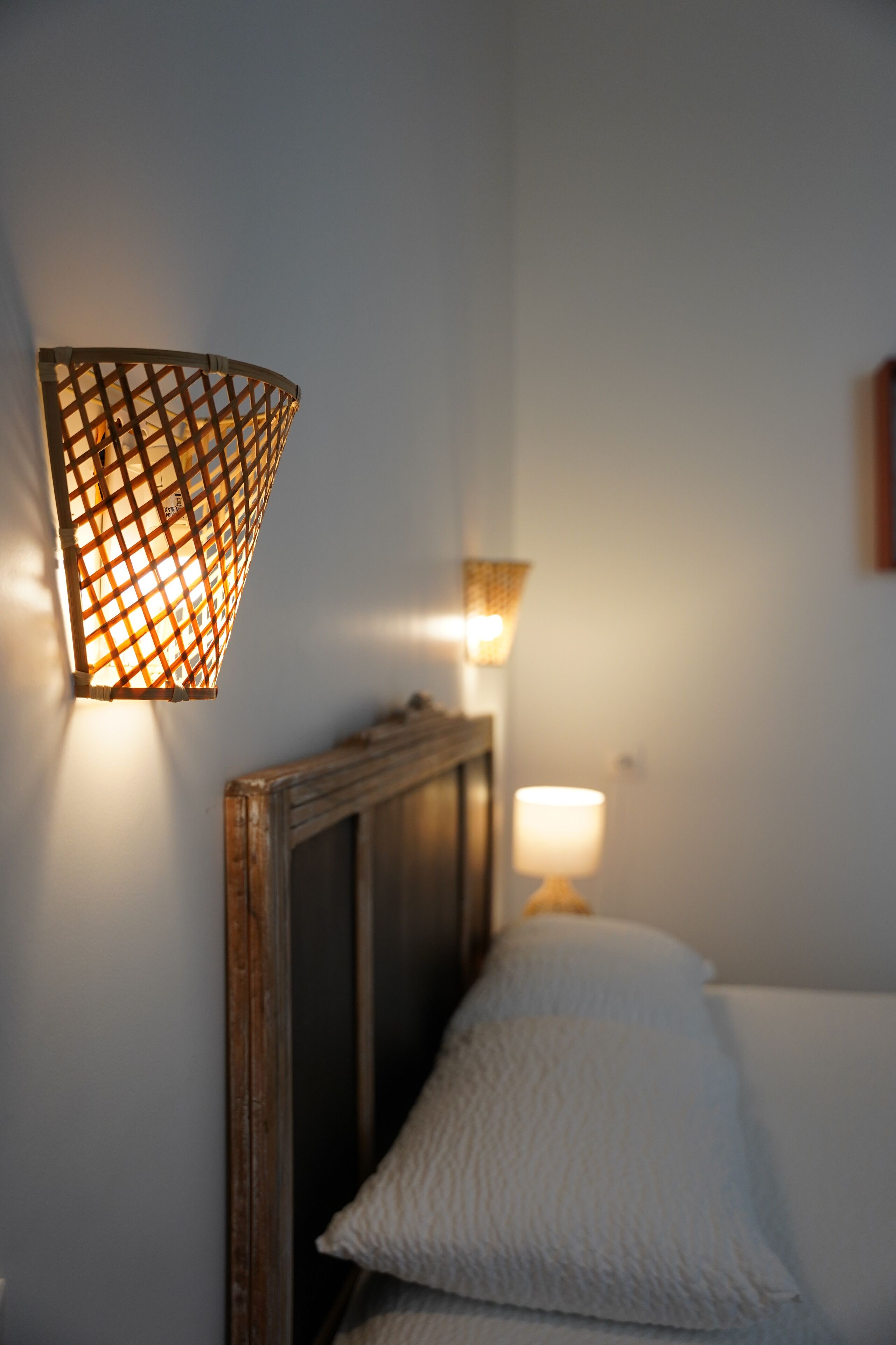 Een slaapkamer met een houten hoofdbord, een wit kussen en een wandlamp.
