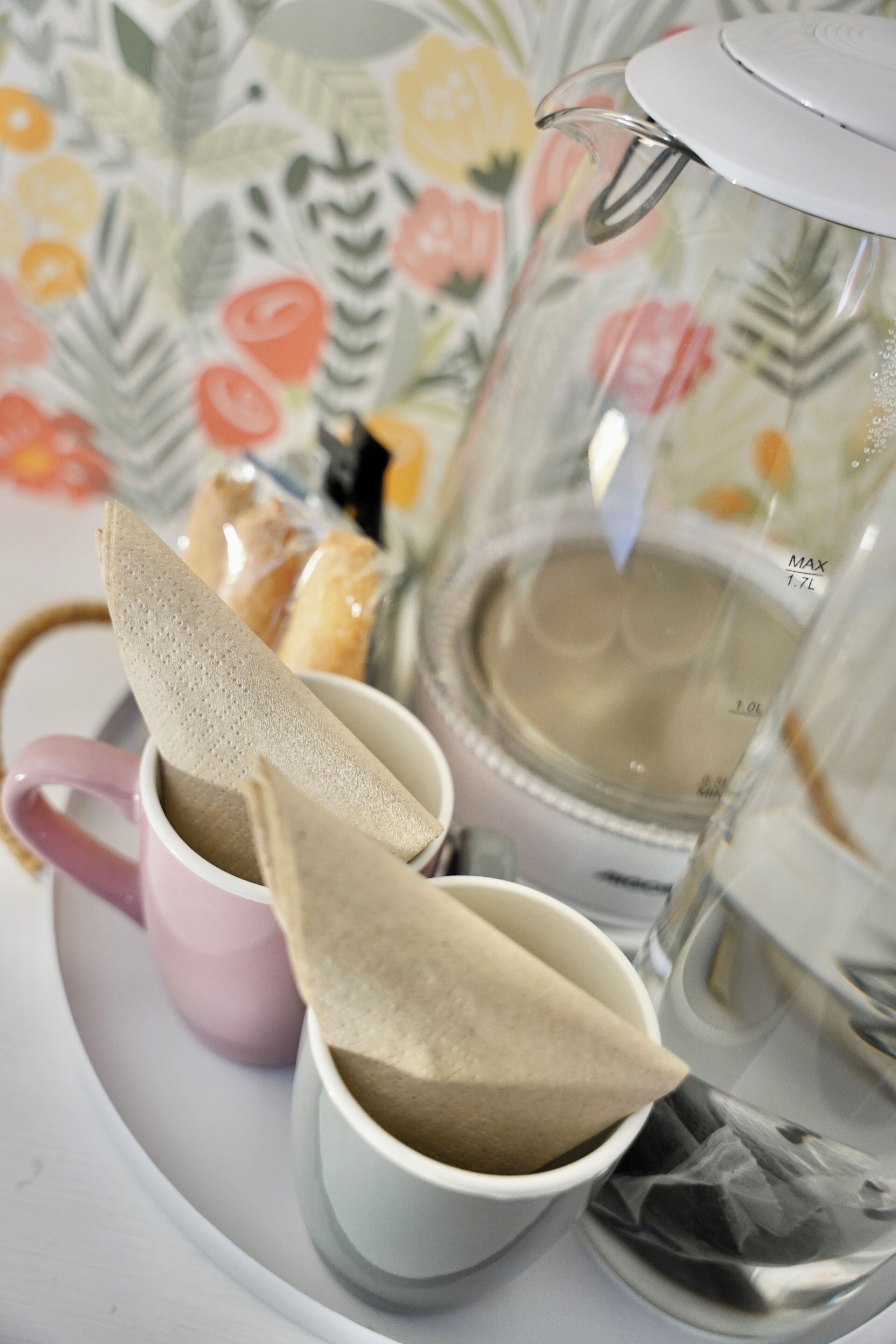 Un plateau avec deux tasses, une rose et une blanche, contenant des sachets de thé et une théière.