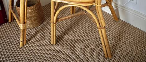 A wicker chair and table with a woven basket underneath, set against a plain wall with a power outlet.