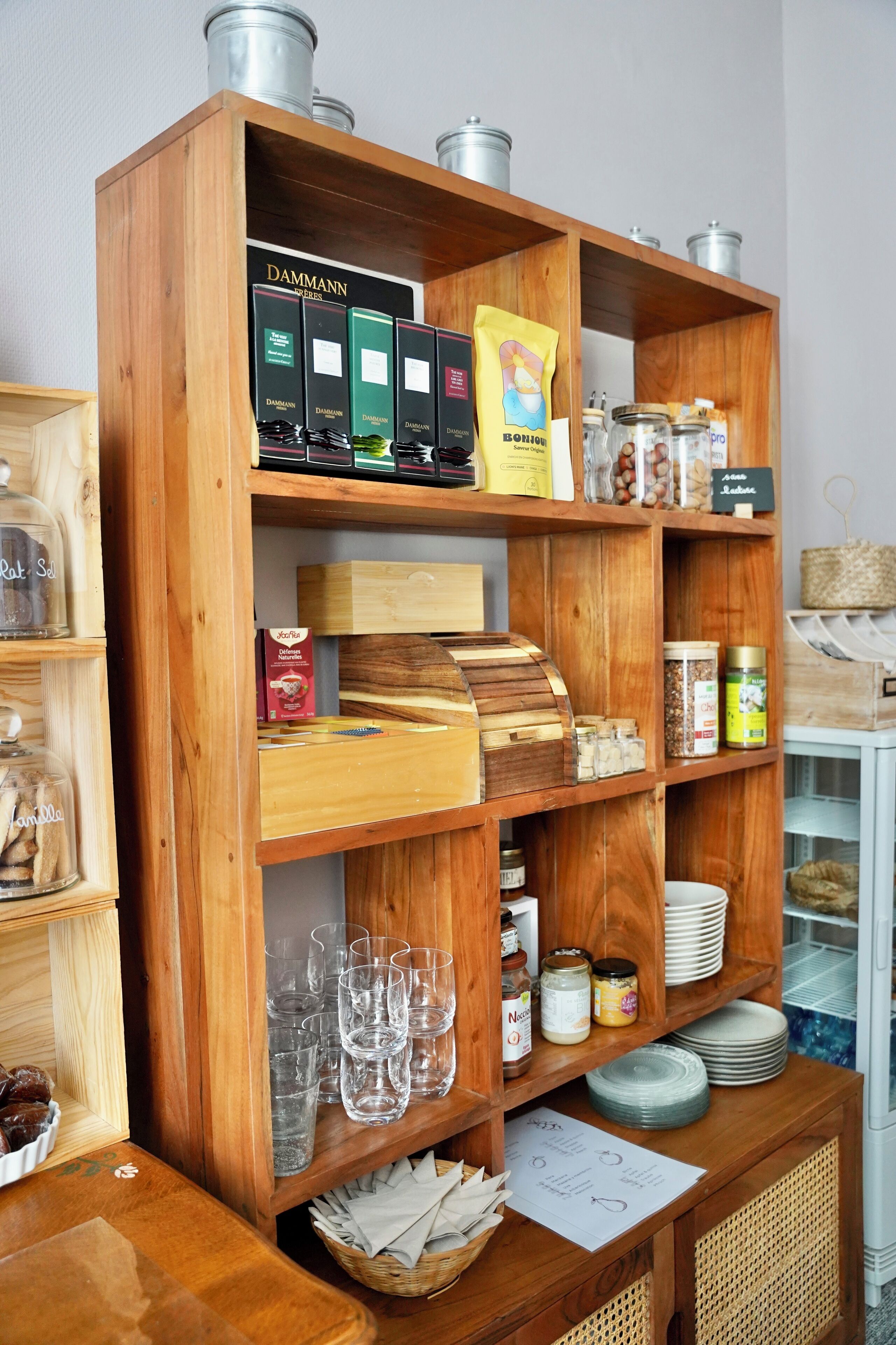 A wooden shelf unit with various food items, glassware, and storage containers.