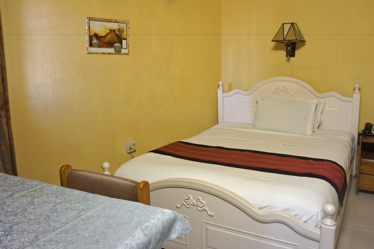 A hotel room with a bed, a bedside table, a lamp, and a painting on the wall.