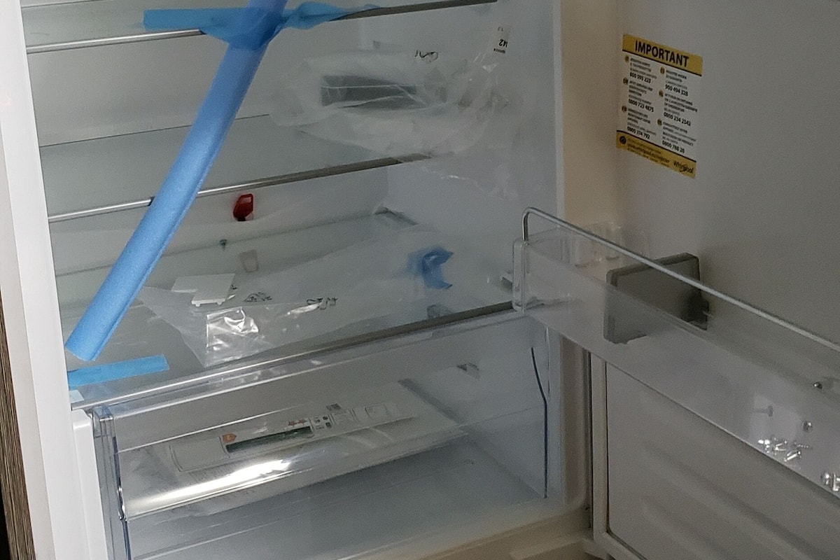 An open refrigerator with a blue tape securing the door, a water dispenser, and a warning label on the door.