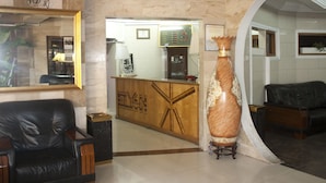 Un hall d’entrée avec un comptoir de réception, un grand vase et un canapé en cuir noir.