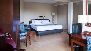 Une chambre d’hôtel avec un lit, deux chaises, une petite table, un bureau et un miroir.
