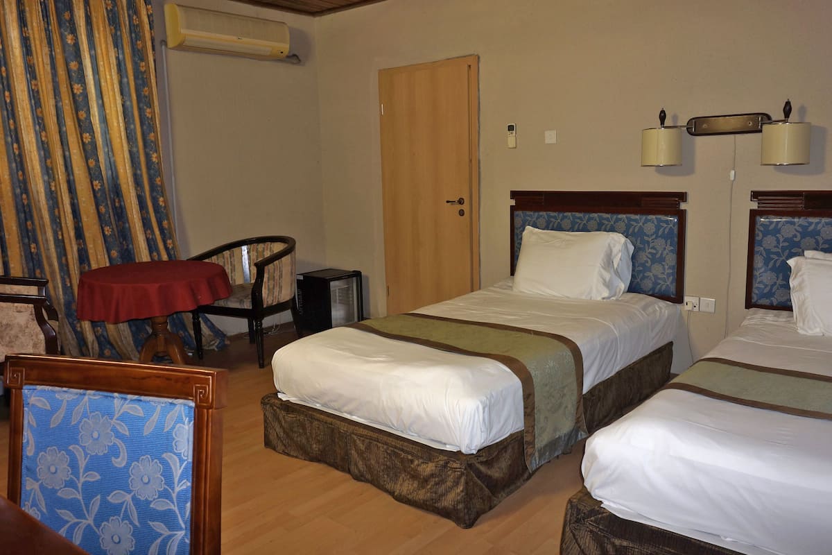 A hotel room with two beds, a desk, a chair, an air conditioner, and a door.
