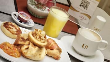 Un plato de desayuno con pasteles, un vaso de jugo de naranja y una taza de café.