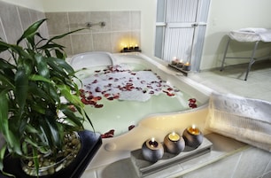 Una bañera con pétalos de rosa, velas y una planta en maceta en un ambiente tipo spa.