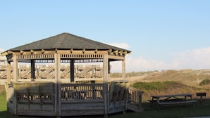 A wooden gazebo with a sloped roof, a bench, and a picnic table. - Sea Gull By Kees Vacations (Hatteras)