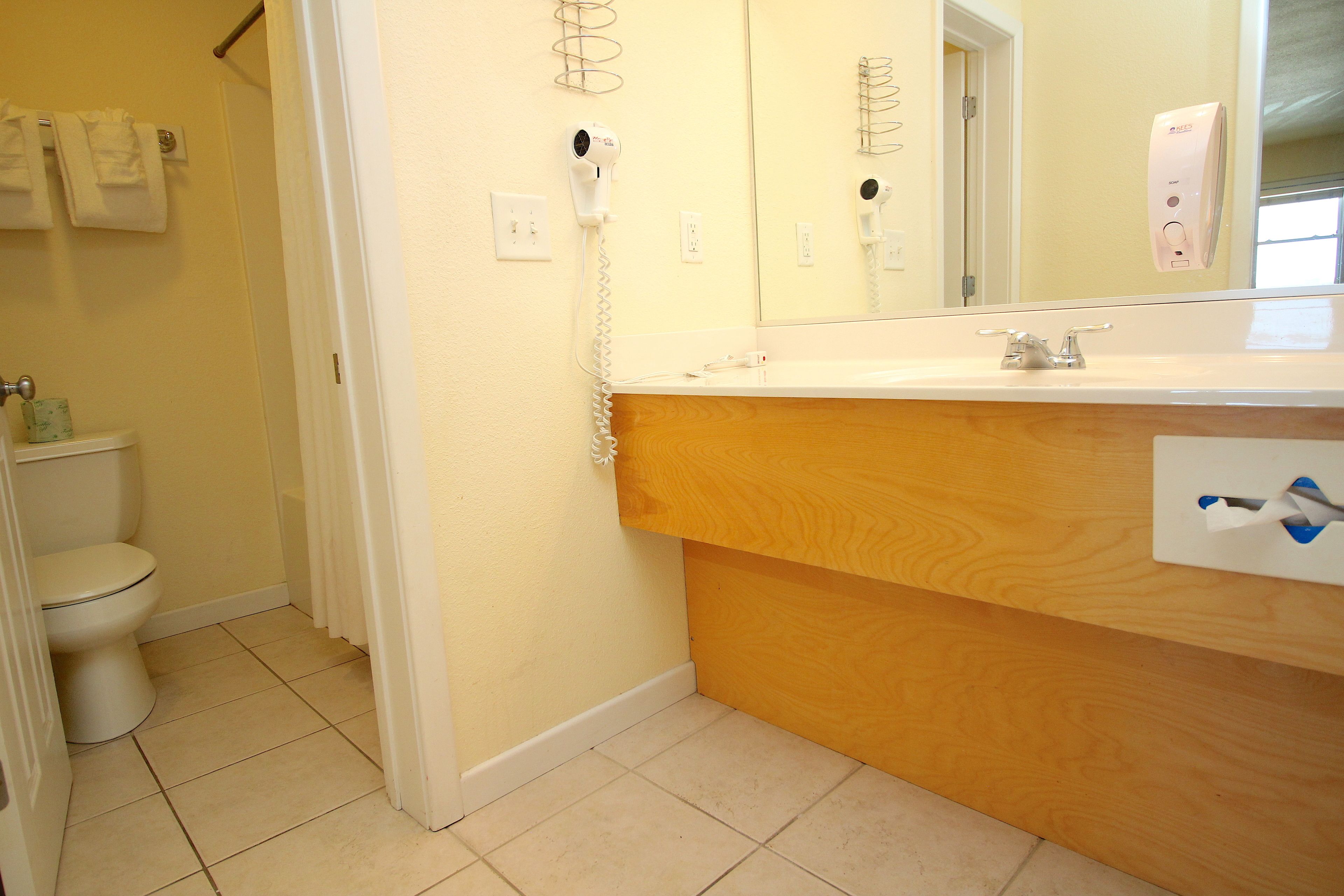 A bathroom with a toilet, a sink with a wooden vanity, a mirror, and a hairdryer mounted on the wall.