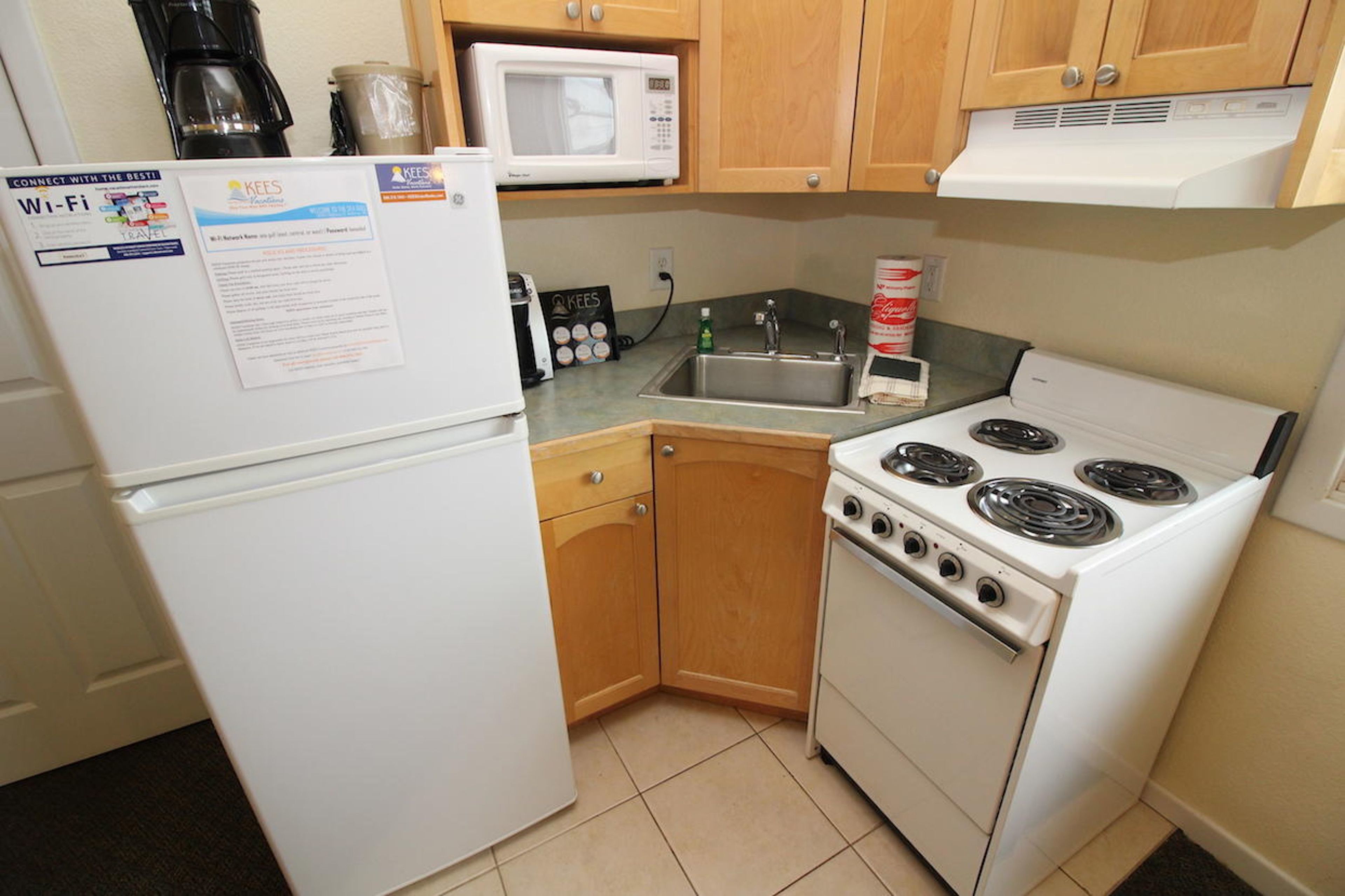 Una cocina compacta con un refrigerador blanco, un microondas, una estufa y armarios de madera.