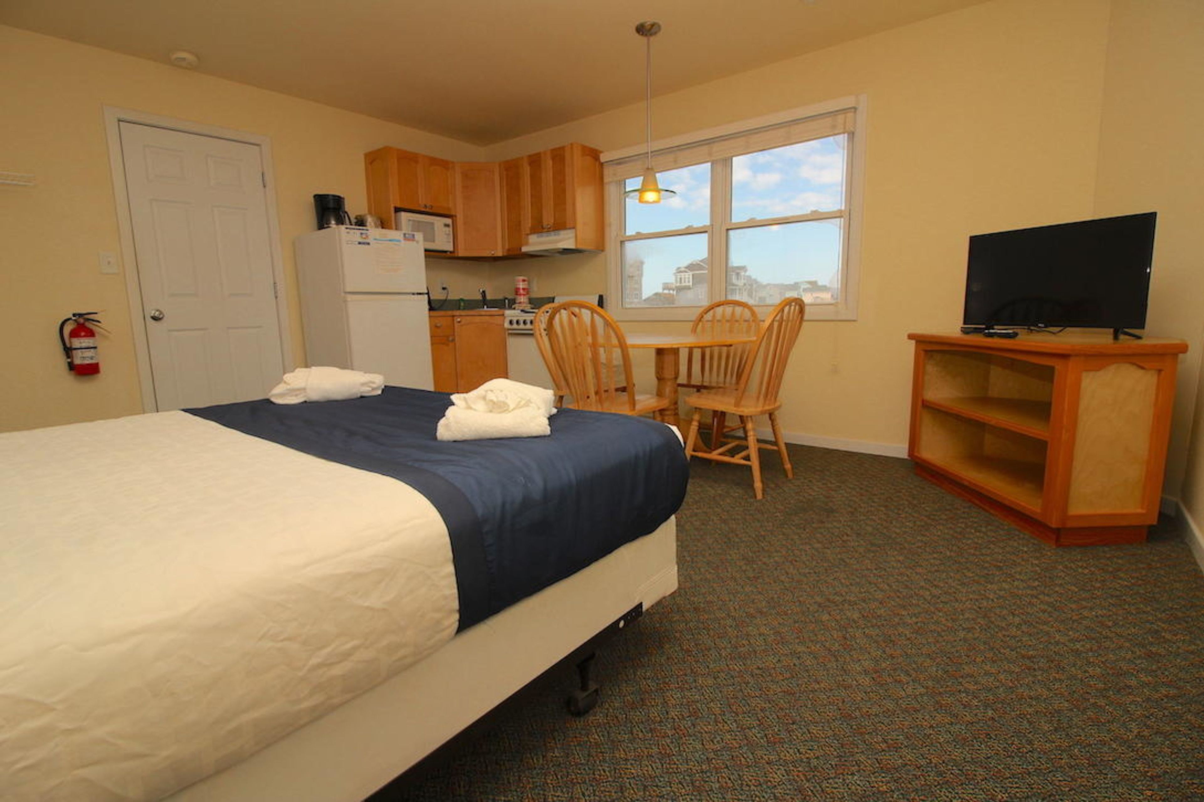 A hotel room with a bed, a desk with a chair, a television on a stand, and a window with a view.