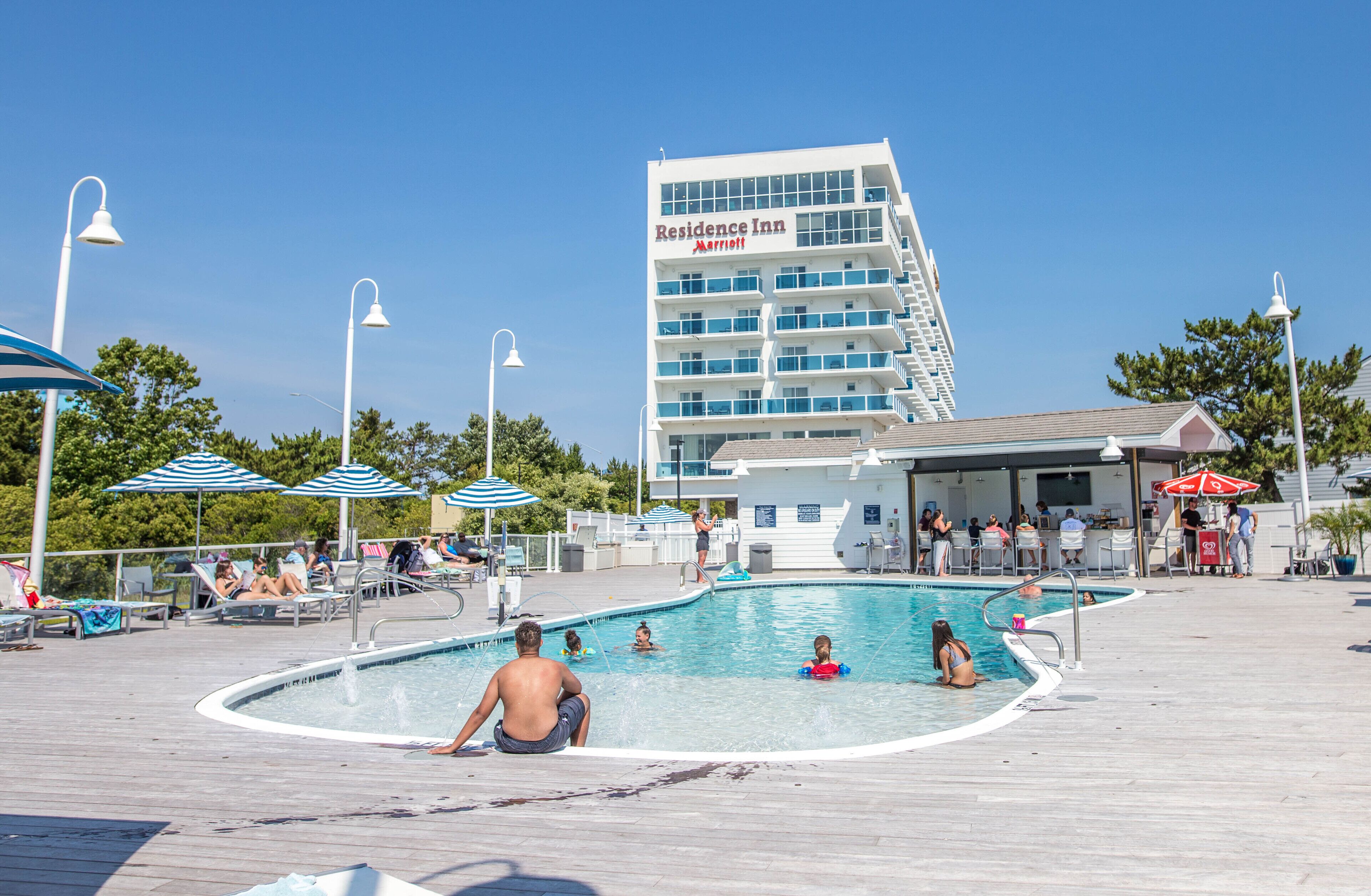 Ein Poolbereich mit Liegestühlen, Sonnenschirmen und einem im Hintergrund sichtbaren Gebäude mit der Aufschrift 'Residence Inn Marriott'.