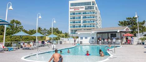Ein Poolbereich mit Liegestühlen, Sonnenschirmen und einem im Hintergrund sichtbaren Gebäude mit der Aufschrift 'Residence Inn Marriott'.