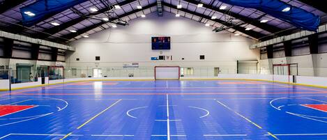 An indoor basketball court with a blue floor, a scoreboard, and a high ceiling with skylights.