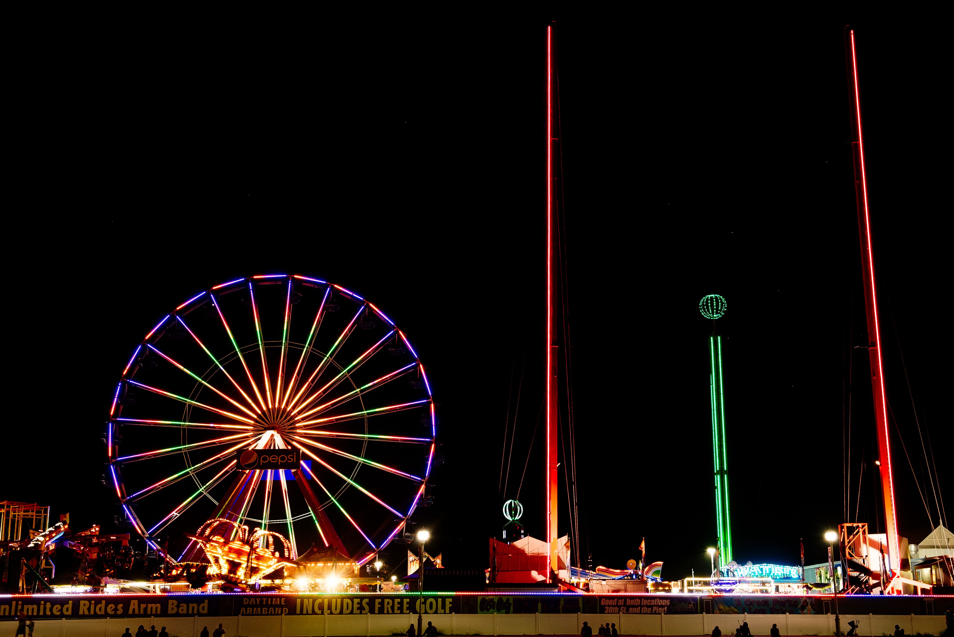 A Ferris wheel with colorful lights and a tall green and red structure in the background.