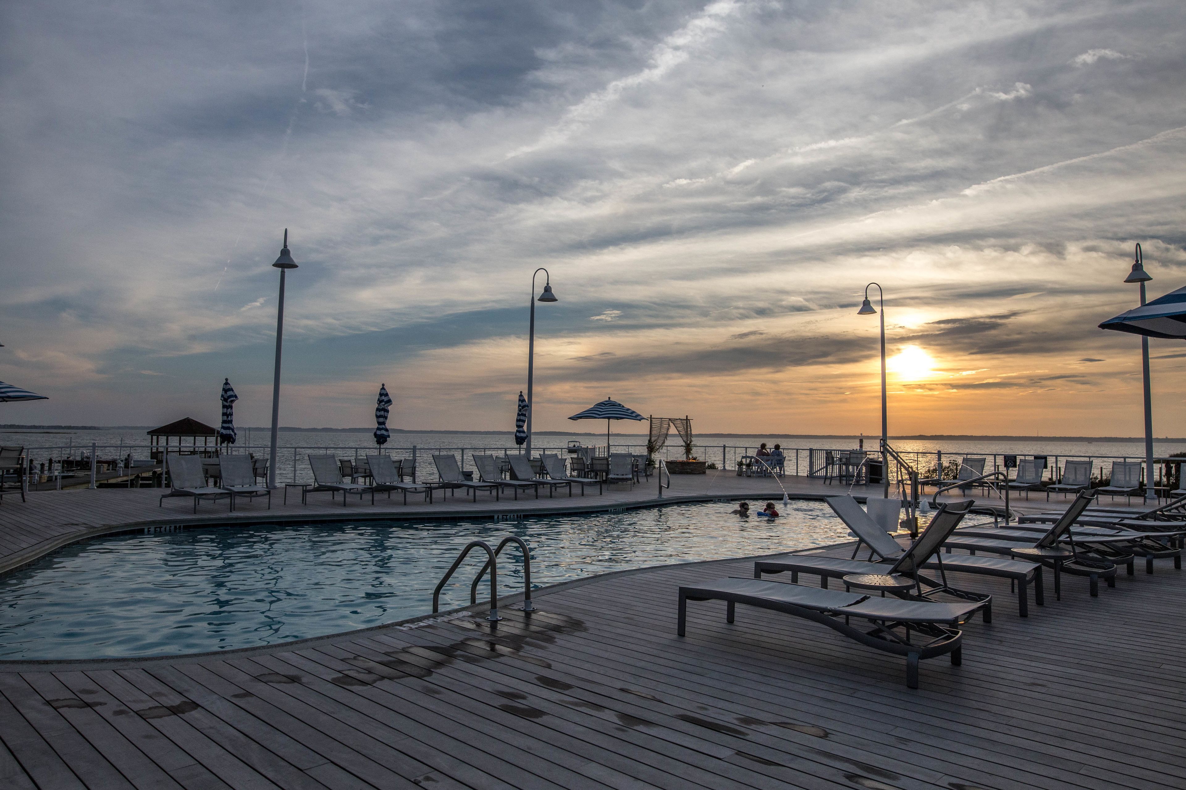 A poolside area with lounge chairs and umbrellas, overlooking the sea during sunset.