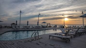 A poolside area with lounge chairs and umbrellas, overlooking the sea during sunset.