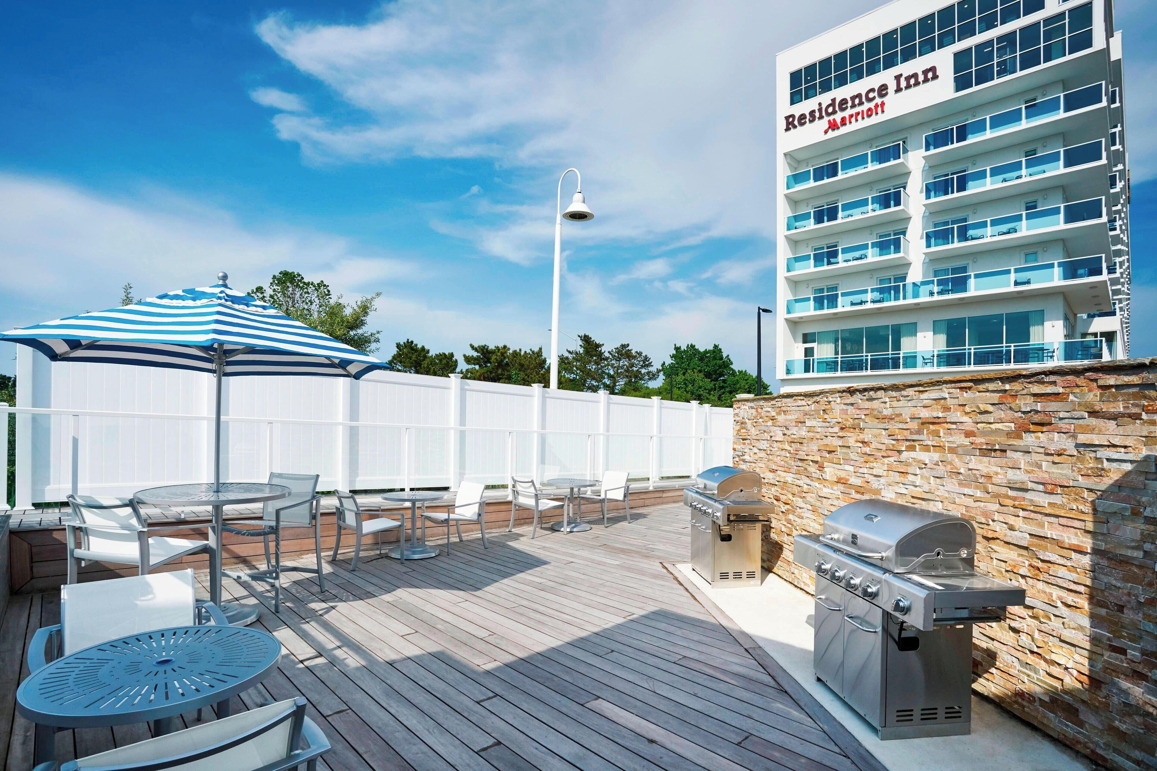 En terrasse med udendørs siddepladser, grill og et Marriott Residence Inn hotel i baggrunden.