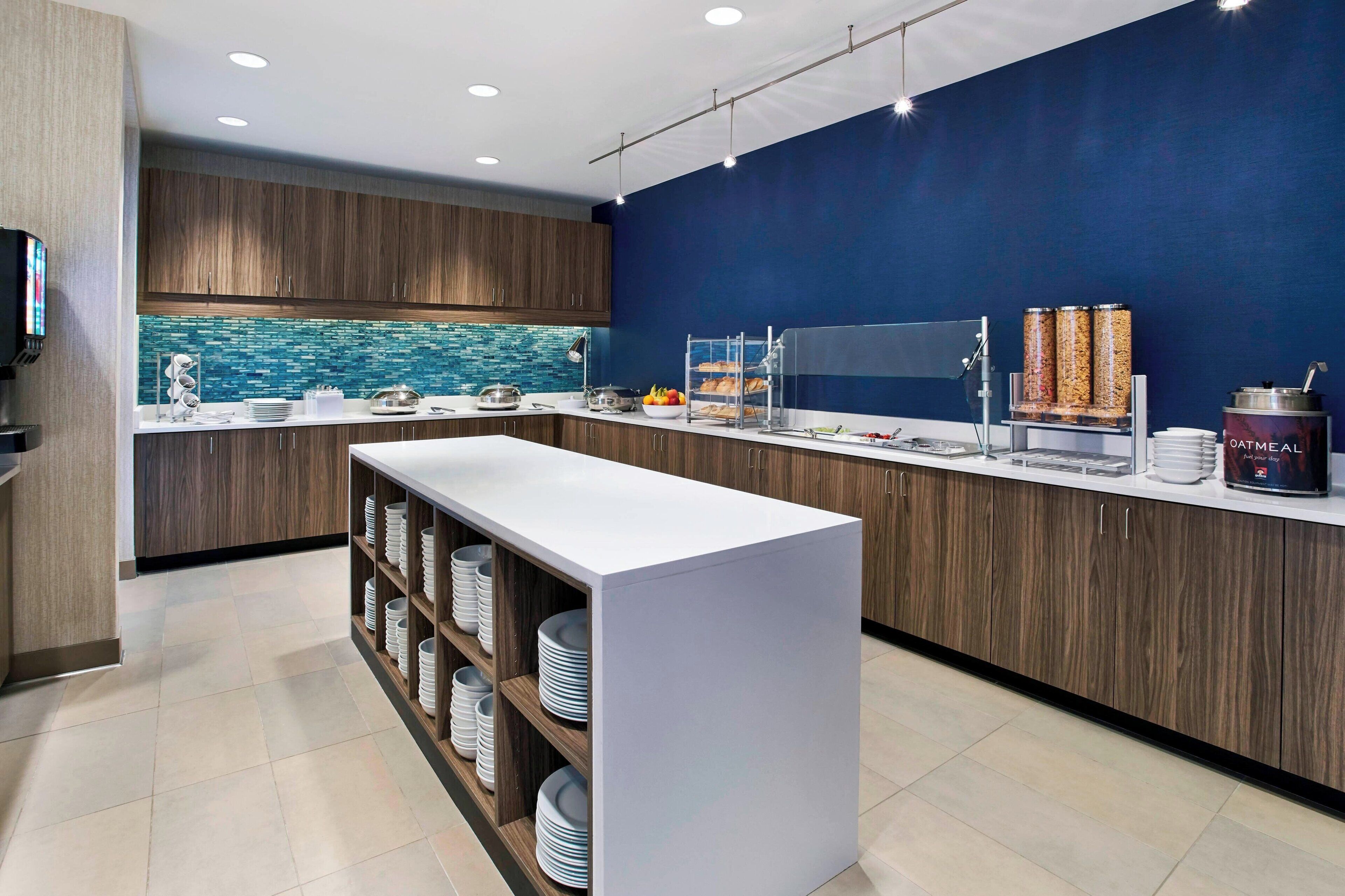 A modern kitchen with wooden cabinets, a white countertop, and a blue accent wall.